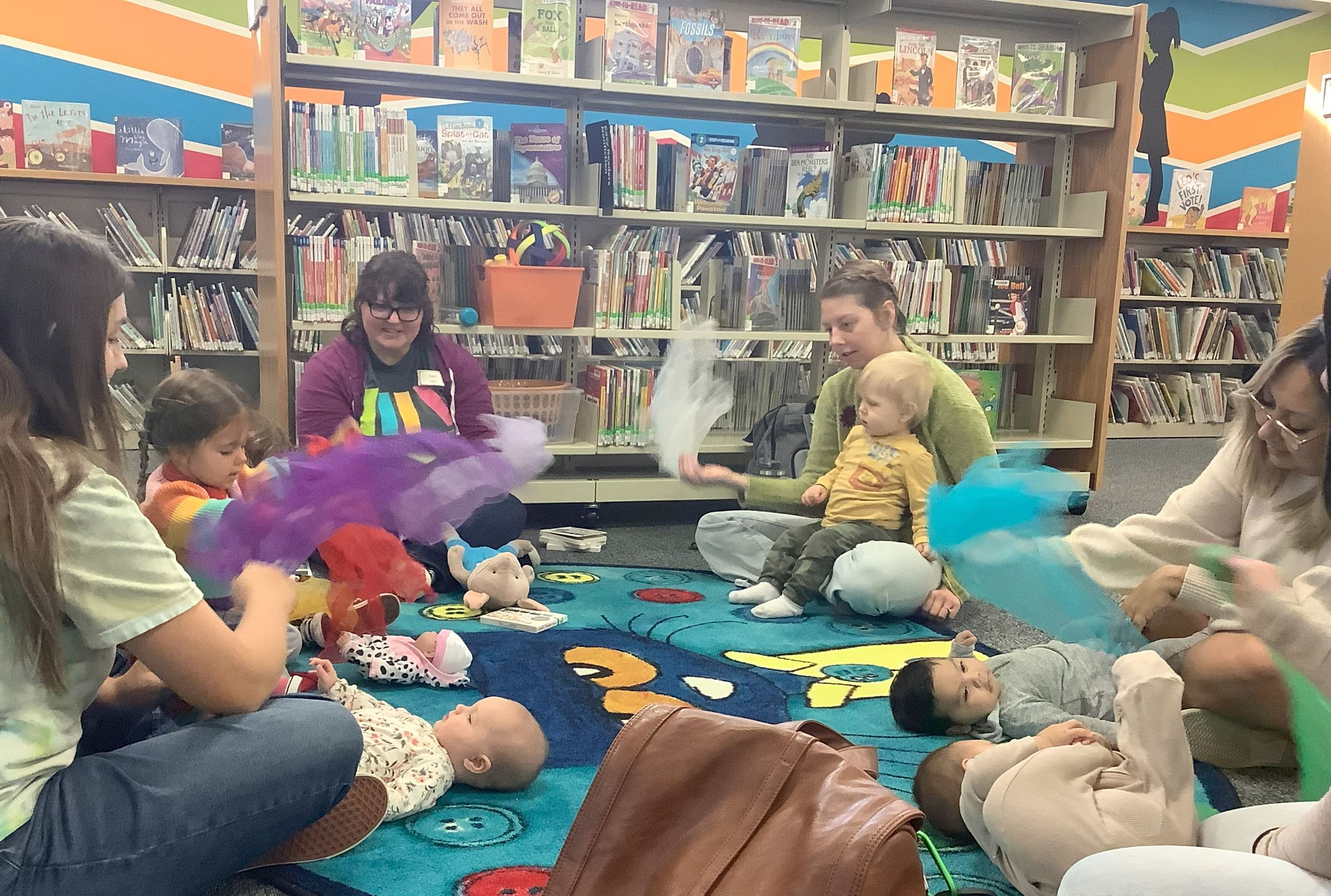 Adults sitting around a rug waving scarves for babies
